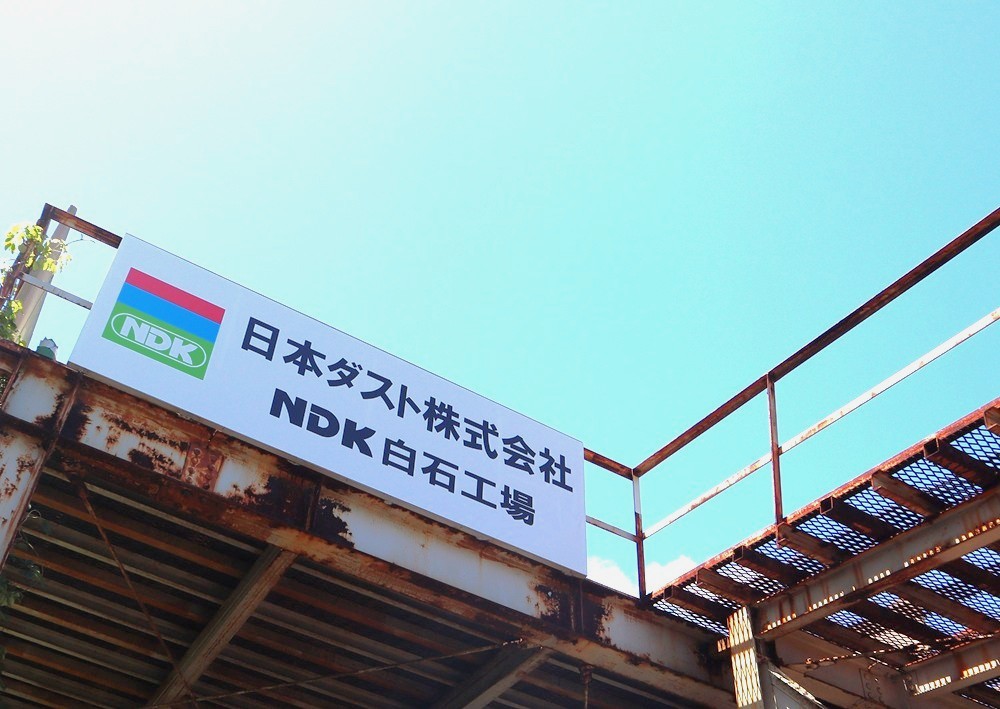 青空の下に掲げられた「日本ダスト株式会社 NDK白石工場」の看板